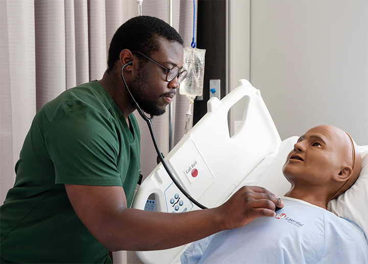 A nursing student practicing using a stethoscope on a manakin.