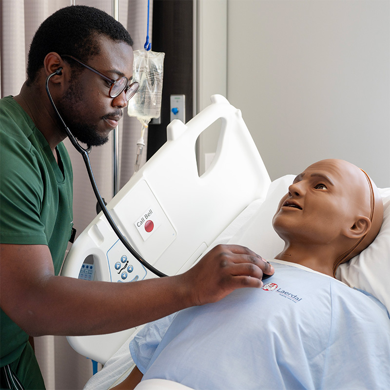 A nursing student practicing using a stethoscope on a manakin.