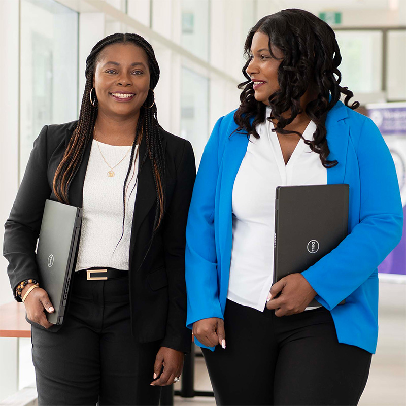 Two nursing graduate students conversing and walking down a hallway.