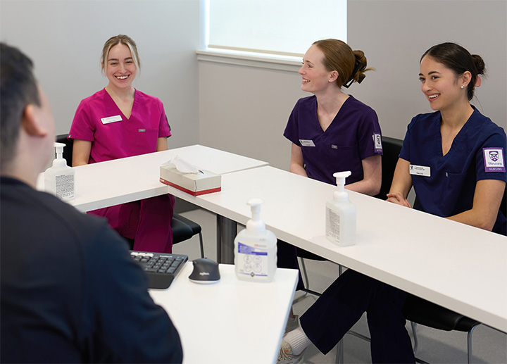 Three nursing students conversing with a professor.
