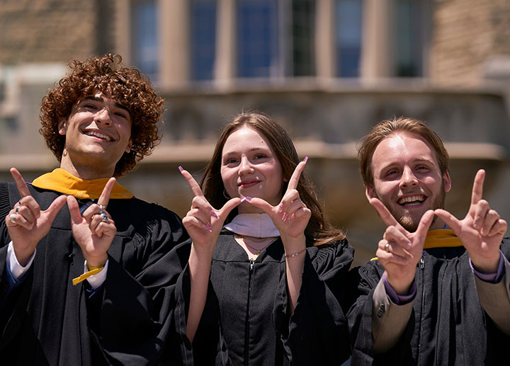 3 graduate students in robe throwing up W signs with their hands