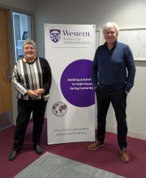 Visiting Fellows Sabine Nolke and John Holmes stand in front of the Western Academy banner