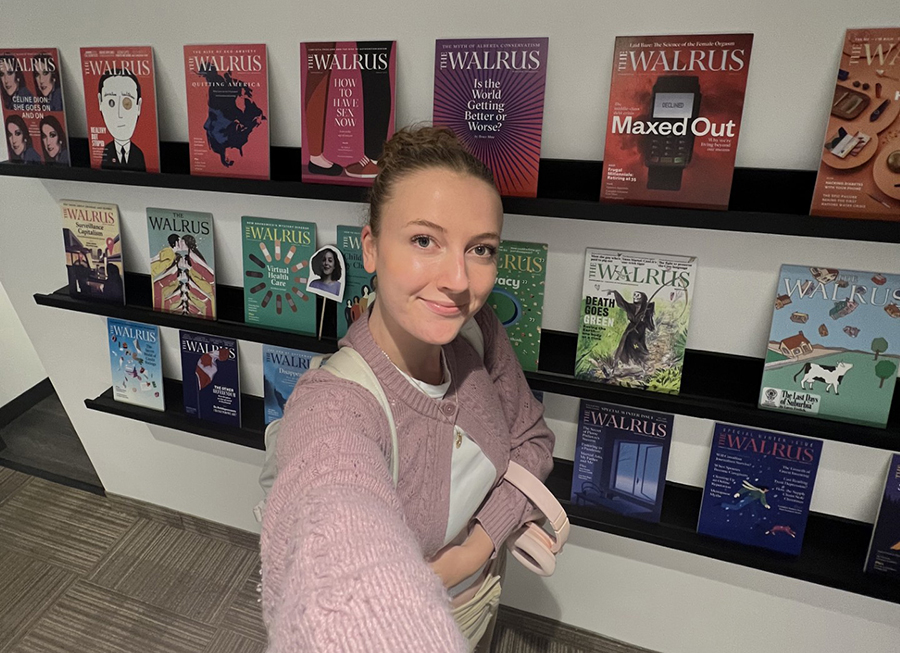  student stands in front of a display of Walrus magazines at the Walrus Offices in Toronto