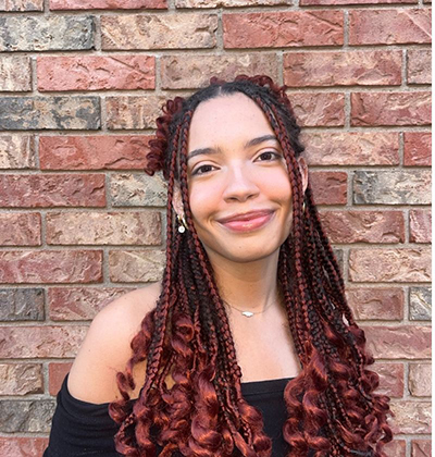A photo of a smiling woman standing in front of a brick wall