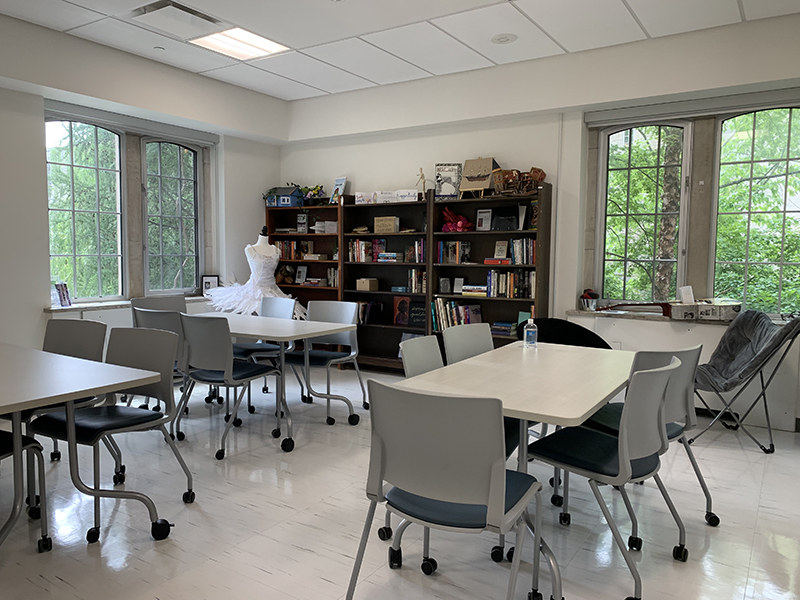 A view of a bright student study room with windows, tables, bookshelf and art