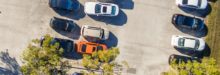 overhead view of a parking lot with some trees and green space to the right of the paved lot.