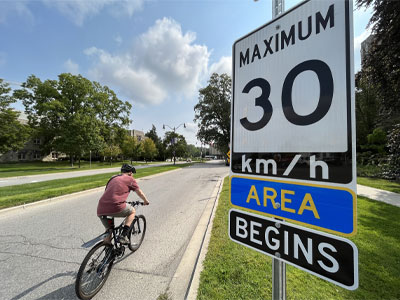 A cyclist is riding on the road into campus beside a 30 kilometre per hour road sign