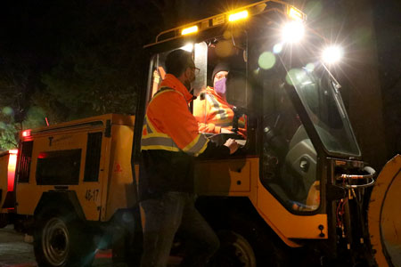 Team members in masks chatting while out on campus is snow clearing machinery