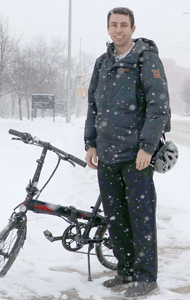 Enrique standing in the snow beside his bike beside Western Road
