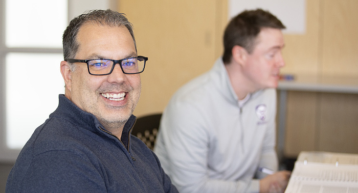 2 men sitting at meeting table. One smiling at camera