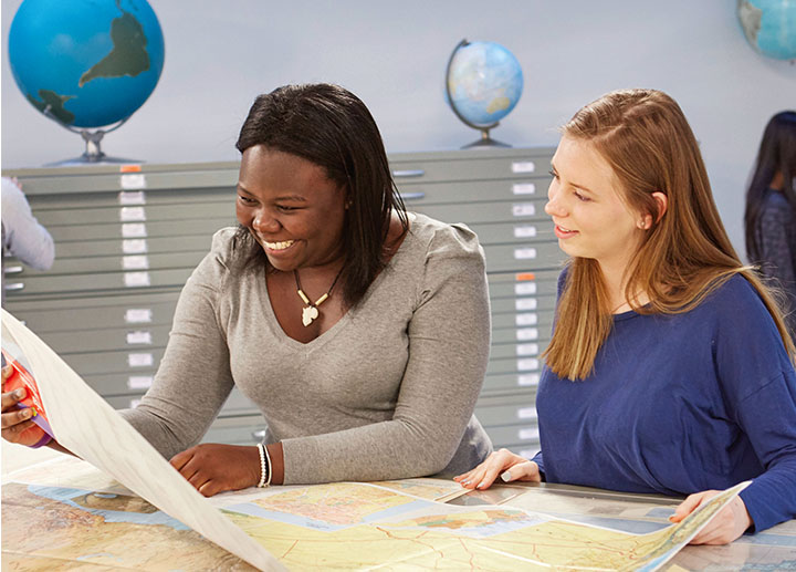 Two women looking at a map together in a classroom