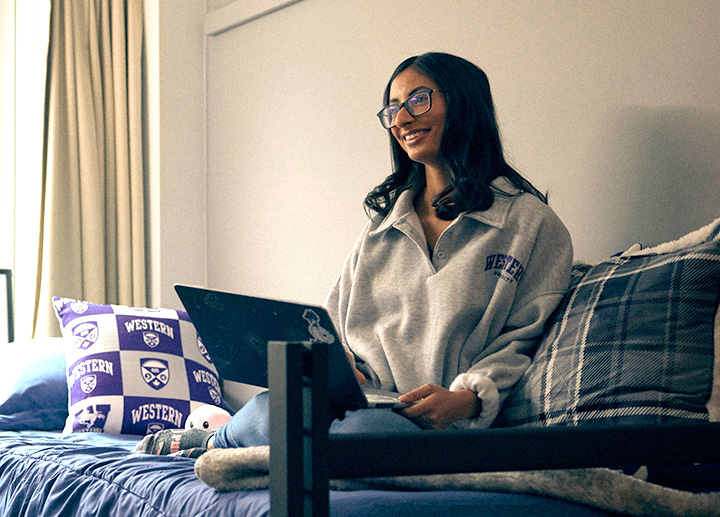 Student sitting on a couch with a laptop and a Western University pillow