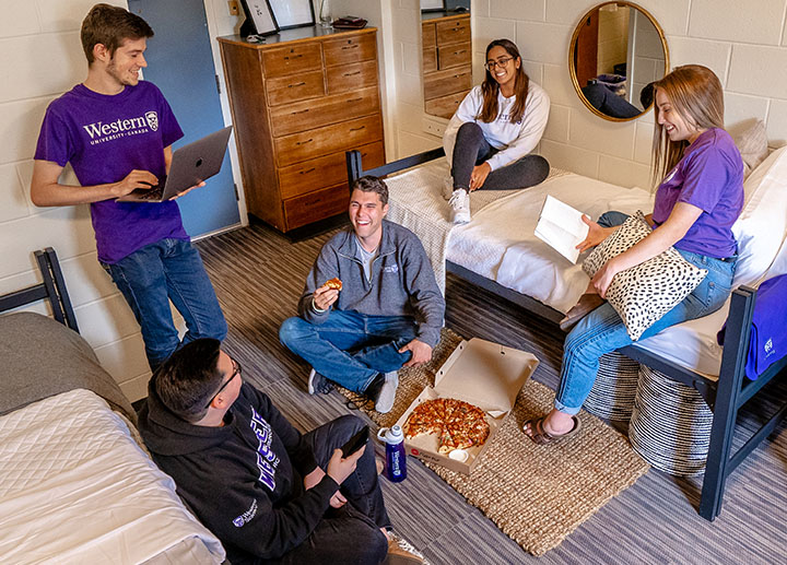 A group of diverse Western student in a dorm eating pizza