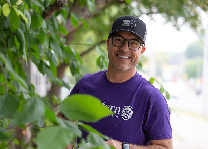 A staff member wearing glasses with a Western University shirt behind a couple plants