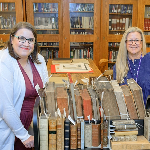 Fourth-year classical studies student Stephanie Leith (left) and Deborah Meert-Williston (right) with horizontal stacks of extremely old books