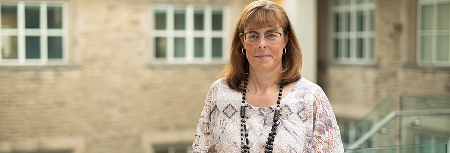 Image of Alison Allan, standing in againts a generic backdrop of out-of-focus stone walls and windows.