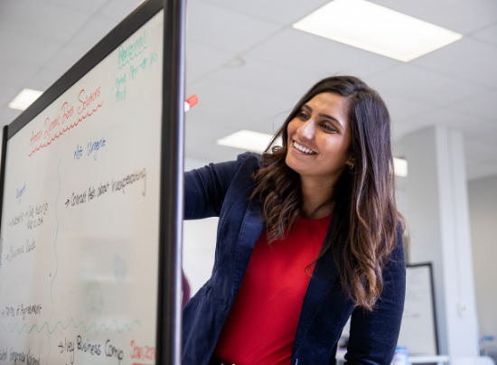 Woman smiling while writing on a whiteboard.