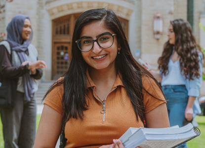 Student holding textbooks stands in front of Middlesex College with two peers in the background