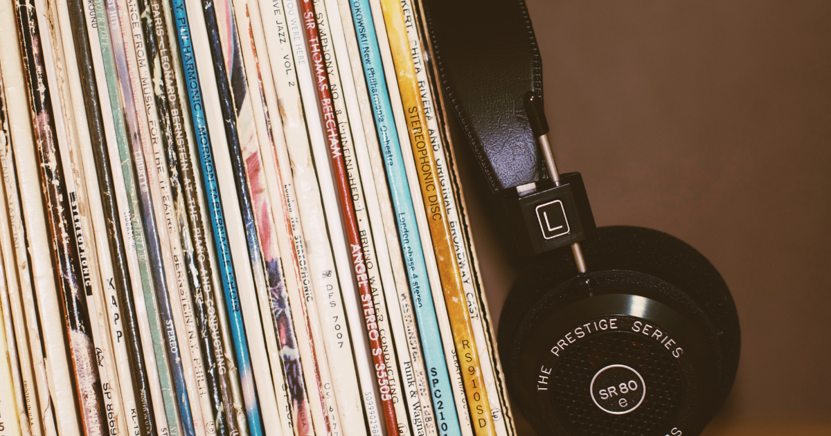 A stack of vinyl records on a shelf next to a pair of headphones