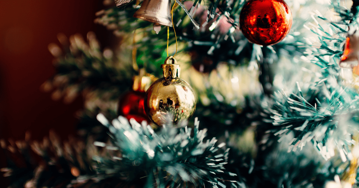 A gold christmas bulb hanging from the branch of a christmas tree