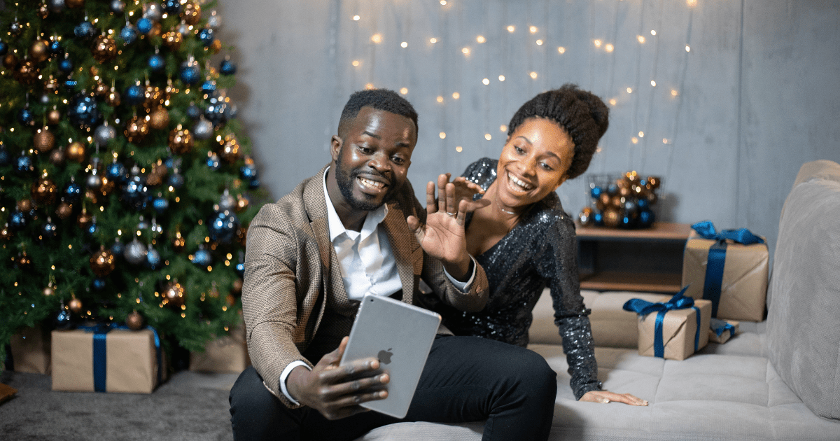 Two people sitting on a couch in front of a christmas tree using an iPad to Zoom