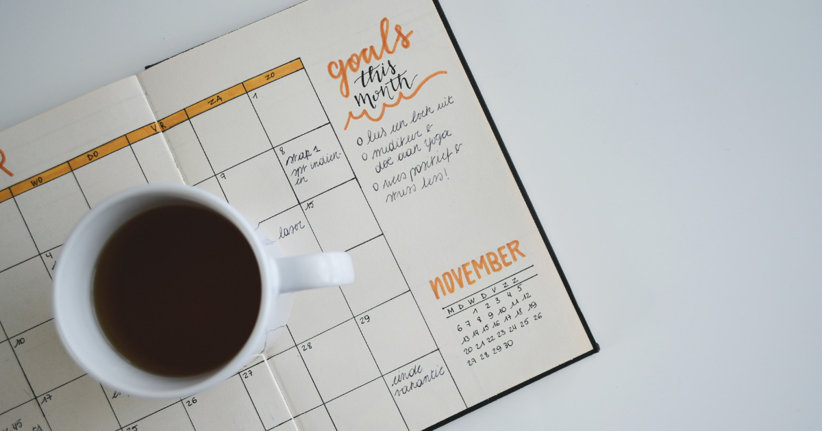 A white coffee mug sitting on top of a journal that contains a list of personal goals for the month