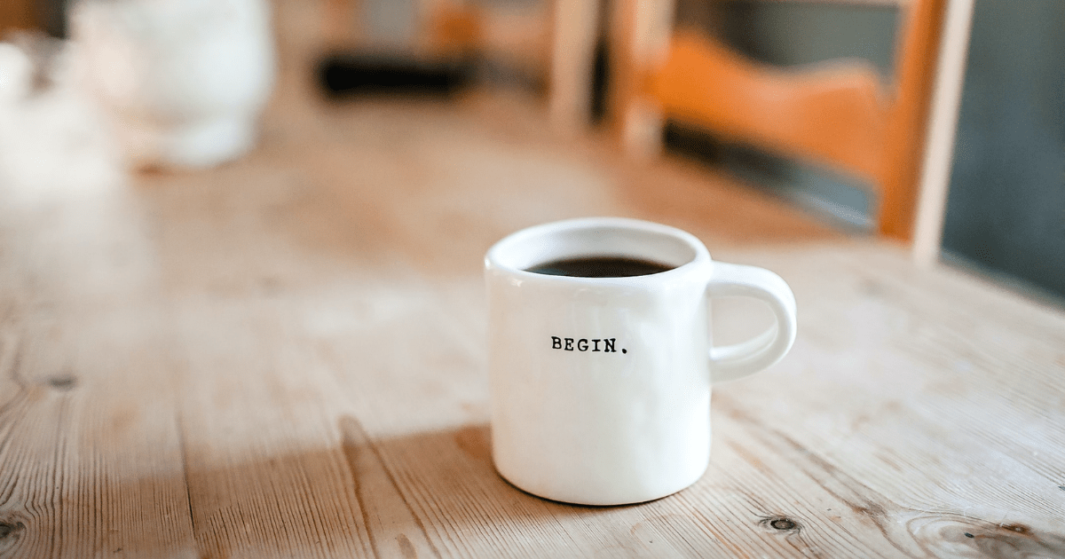 a white ceramic mug sitting with the word begin engraved on it on a wooden table 