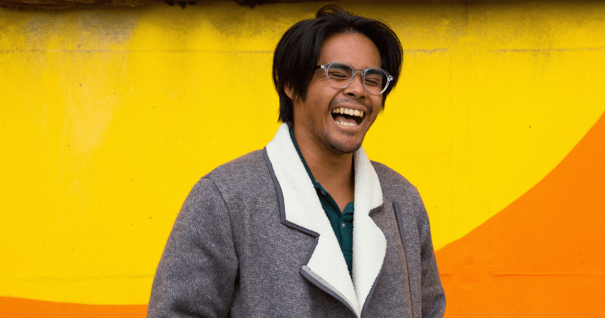 A person standing infront of a bright yellow wall and laughing 