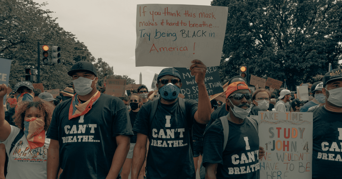 Photo of a man at a Black Lives Matter Protest holding a sign reading: If you think this mask makes it hard to breathe, try being Black in America