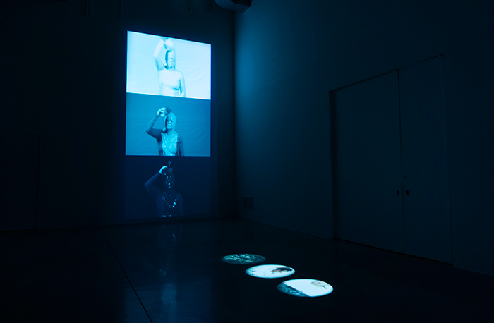 An installation view of Sepideh Dashti's exhibition, showing a large-scale video work on the wall and three spotlight videos on the floor