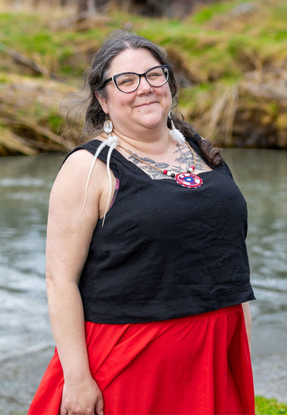 Indigenous artist Jenn Plourde standing in front of a river with a forest in the background